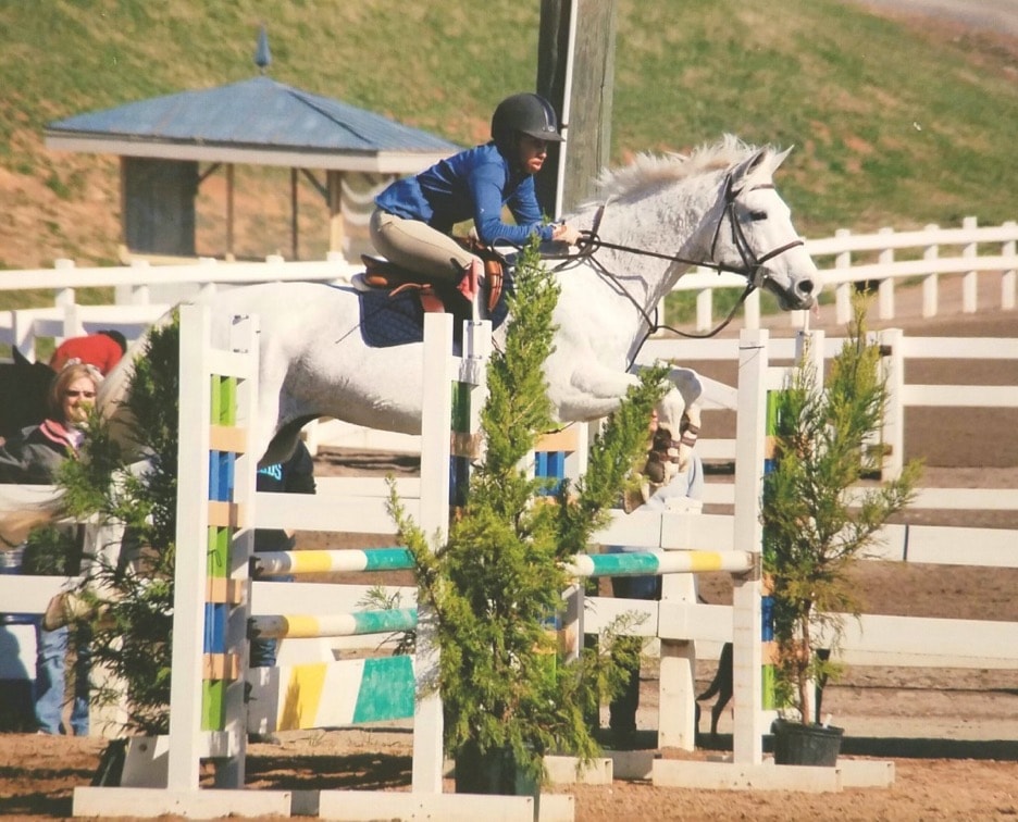 Kristen Johnson jumping a white horse at an equestrian event