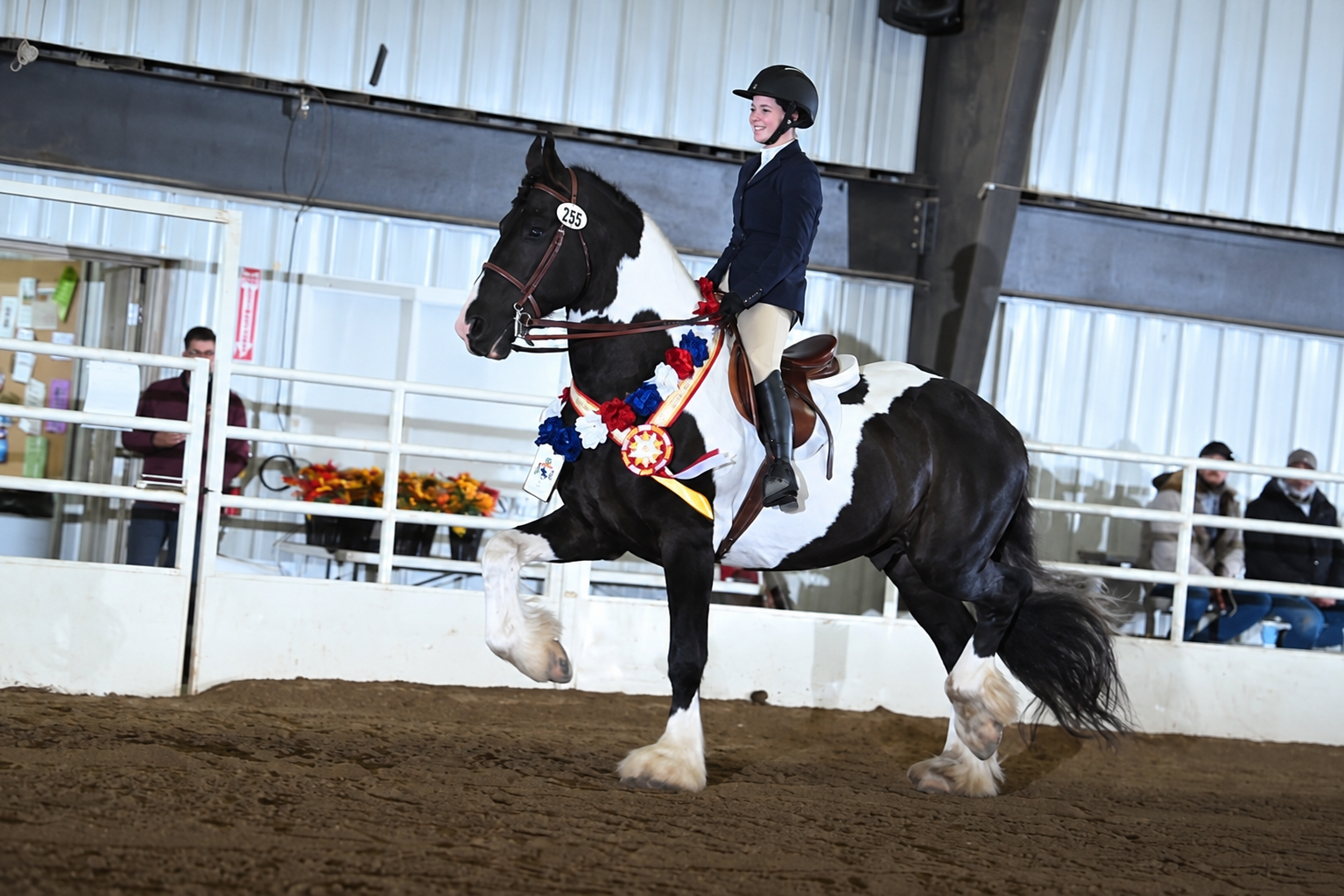Taylor riding a pinto horse at an indoor equestrian competition